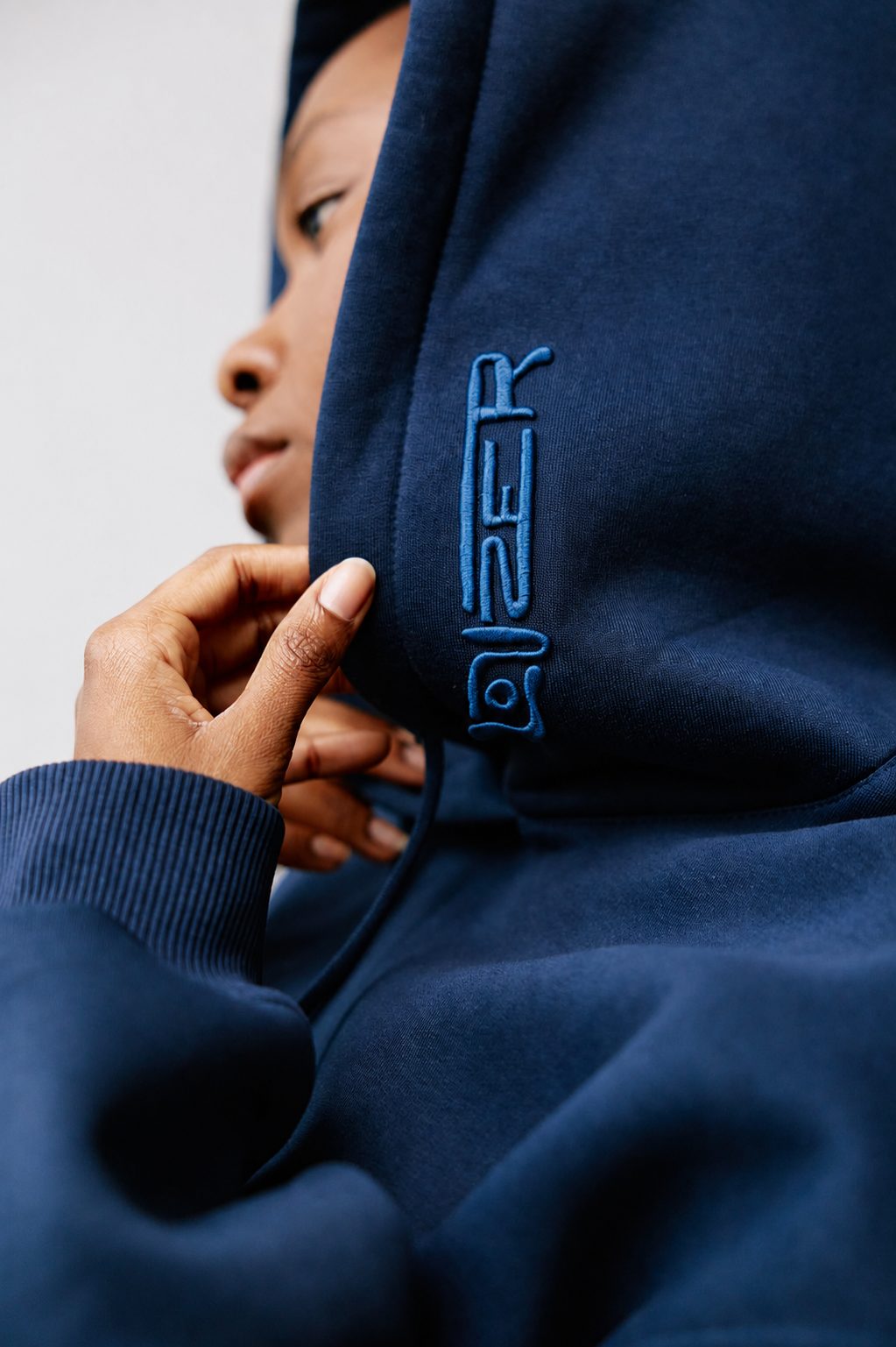 Close view of a hand holding the navy hood, showing the raised embroidered lockup