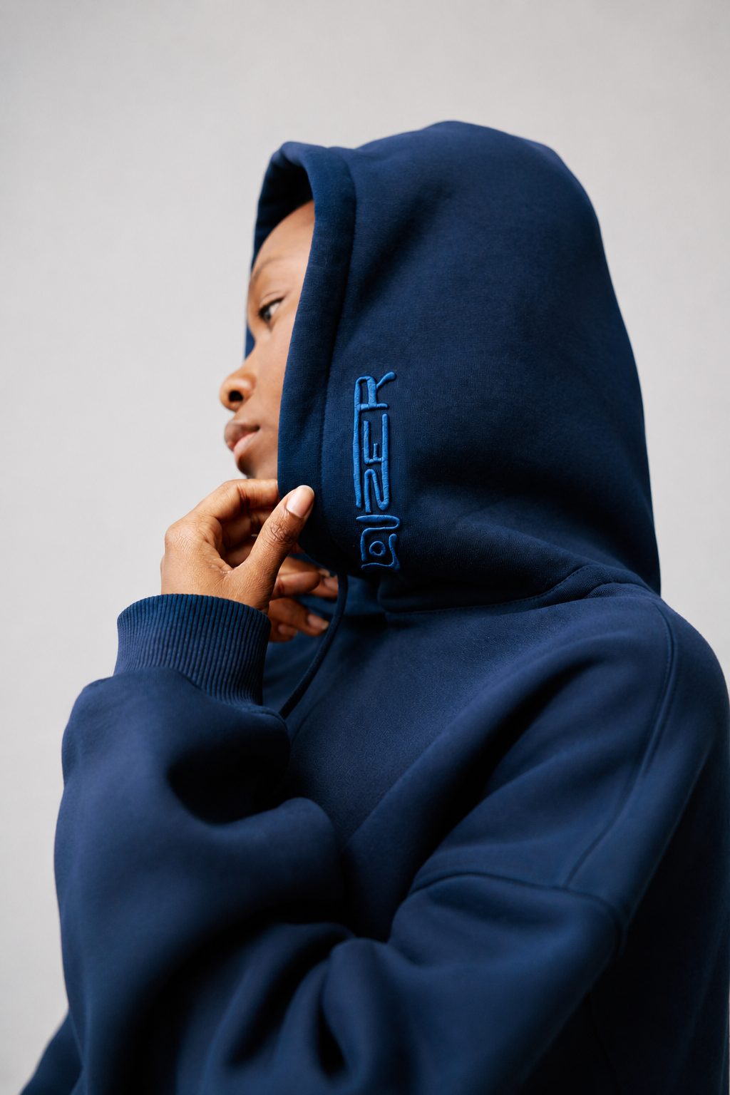 A person wearing a navy hood with the LOUZER mark embroidered vertically along the hood placket