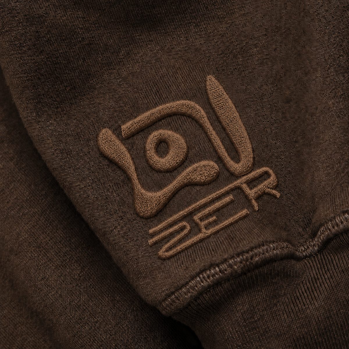 Tonal brown embroidery of the LOUZER sigil on a brown sleeve cuff