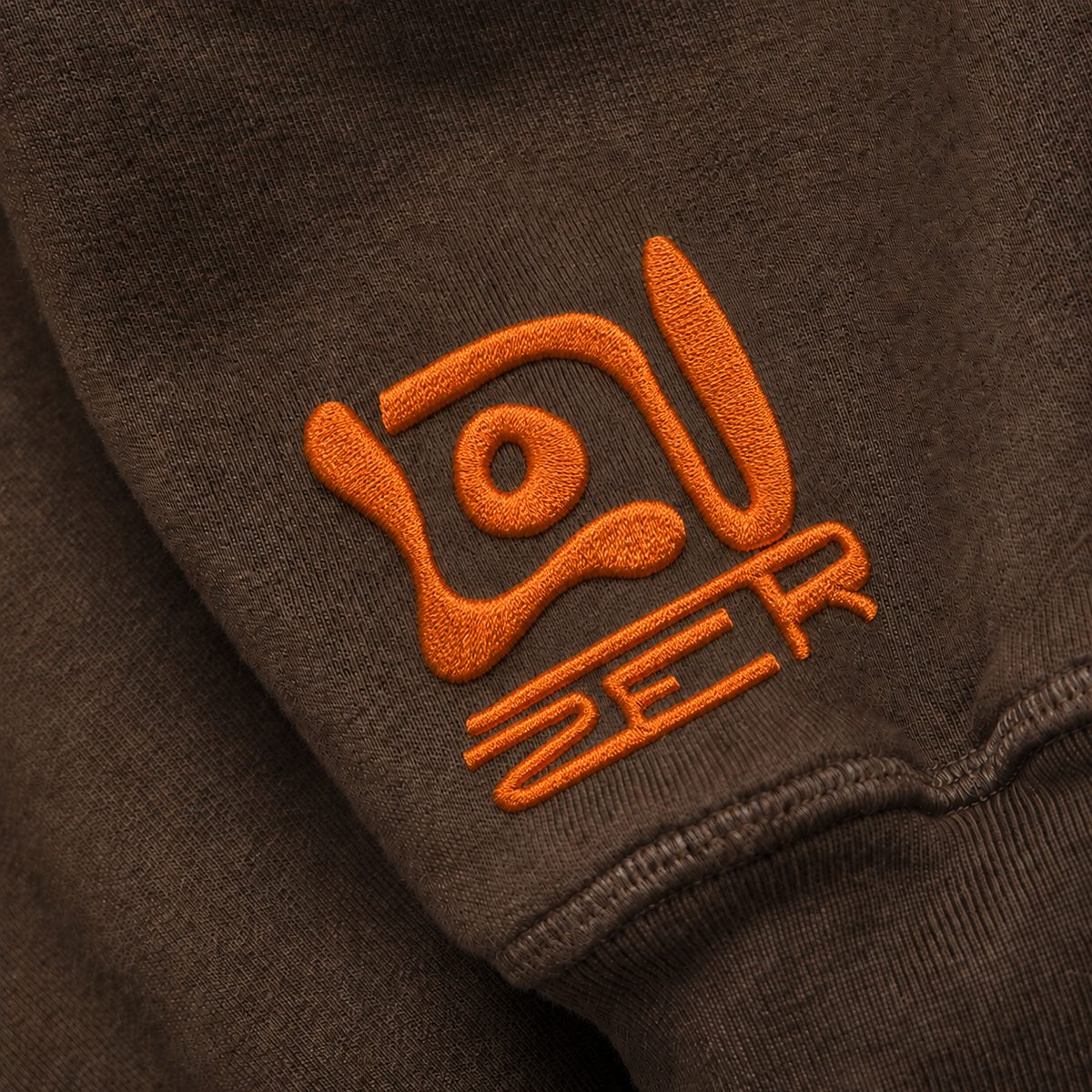 Orange thread embroidery of the LOUZER sigil on a brown sleeve